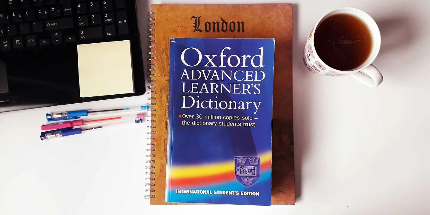 Englisches Wörterbuch auf Tisch neben PC und Tee