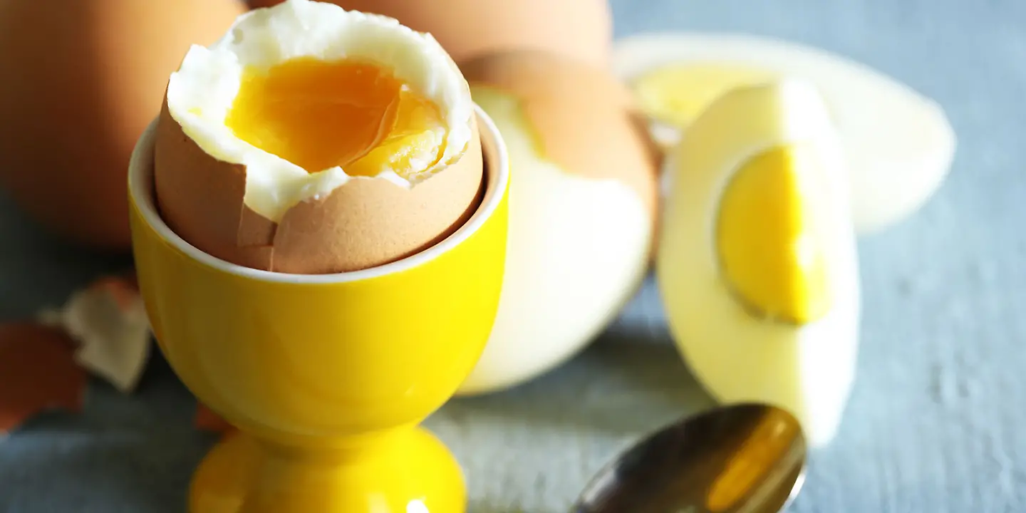 Aufgeschlagenes Frühstücksei in Eierbecher neben weiteren Eiern