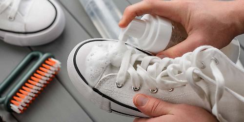 Person putzt weiße Sneaker mit Putzmittel