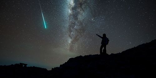 Mann schaut Sternschnuppen und Milchstraße bei Nacht an