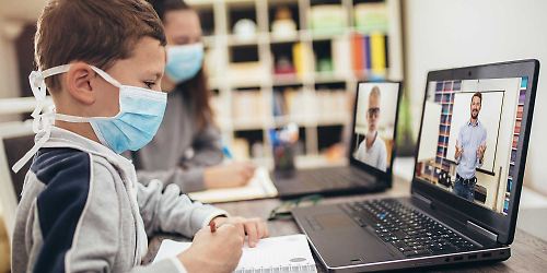 Junge und Mädchen lernen in der Coronakrise mit Masken vor PC